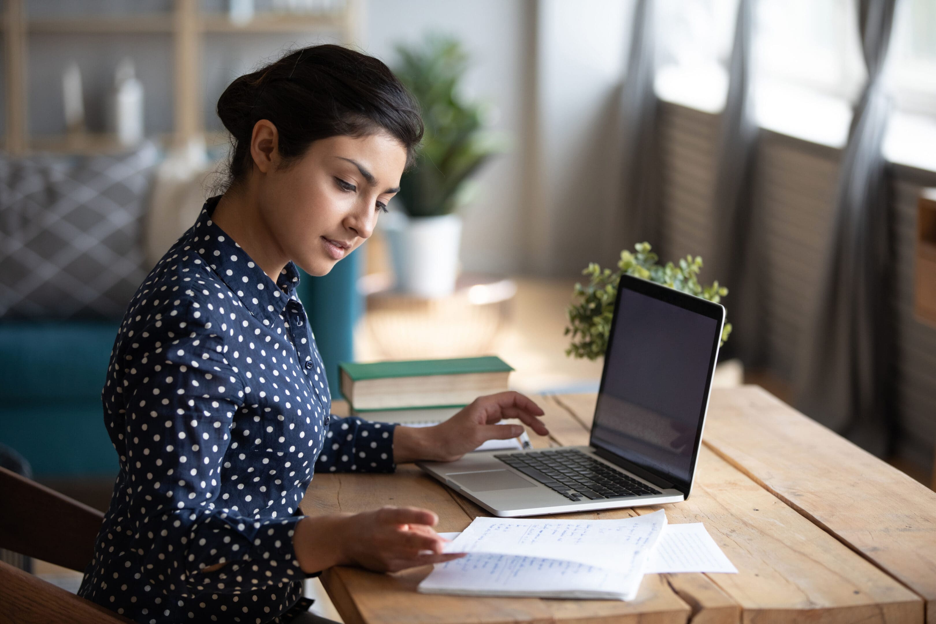 A woman sitting at a table with papers and a laptop.