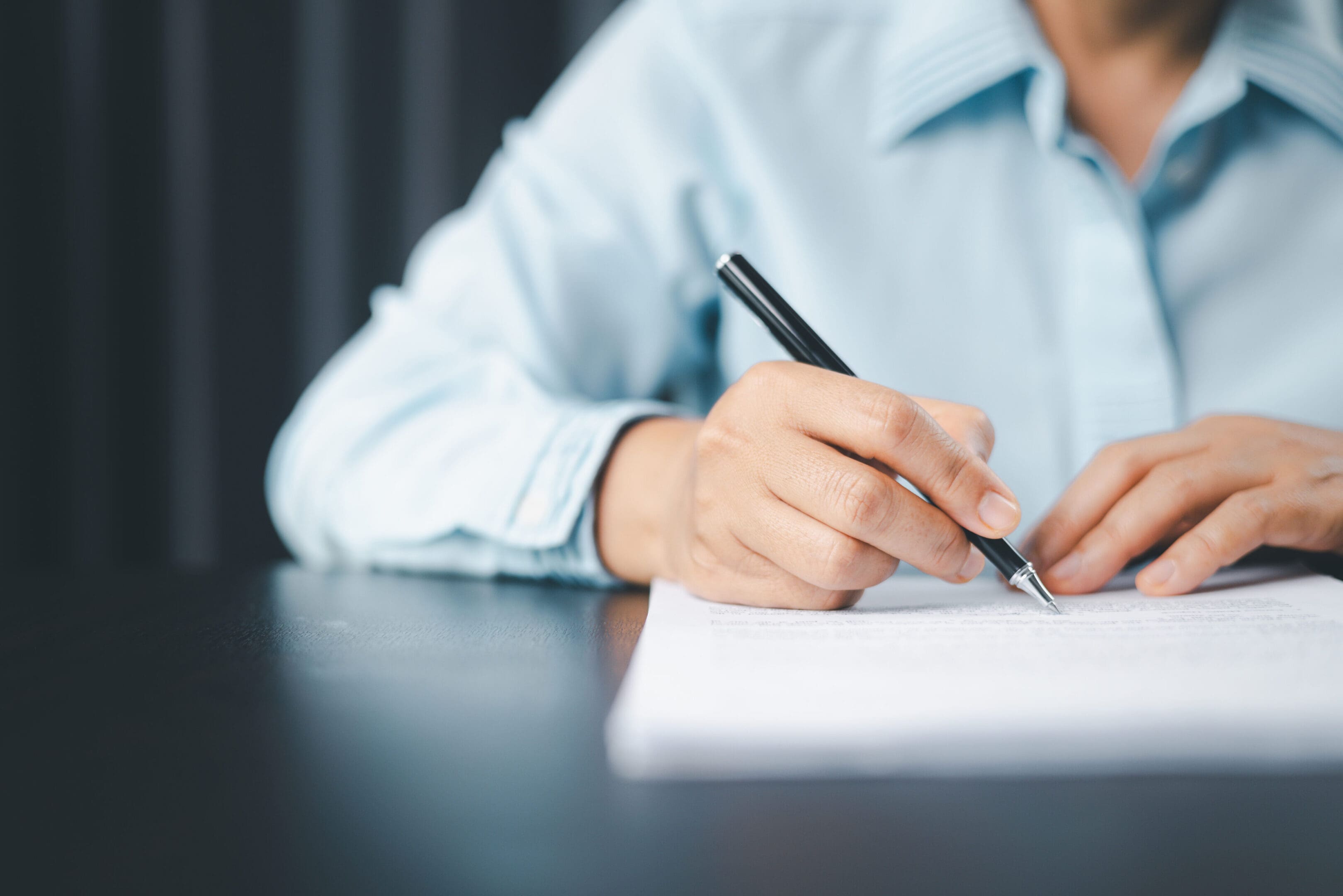 A person writing on paper with a pen.