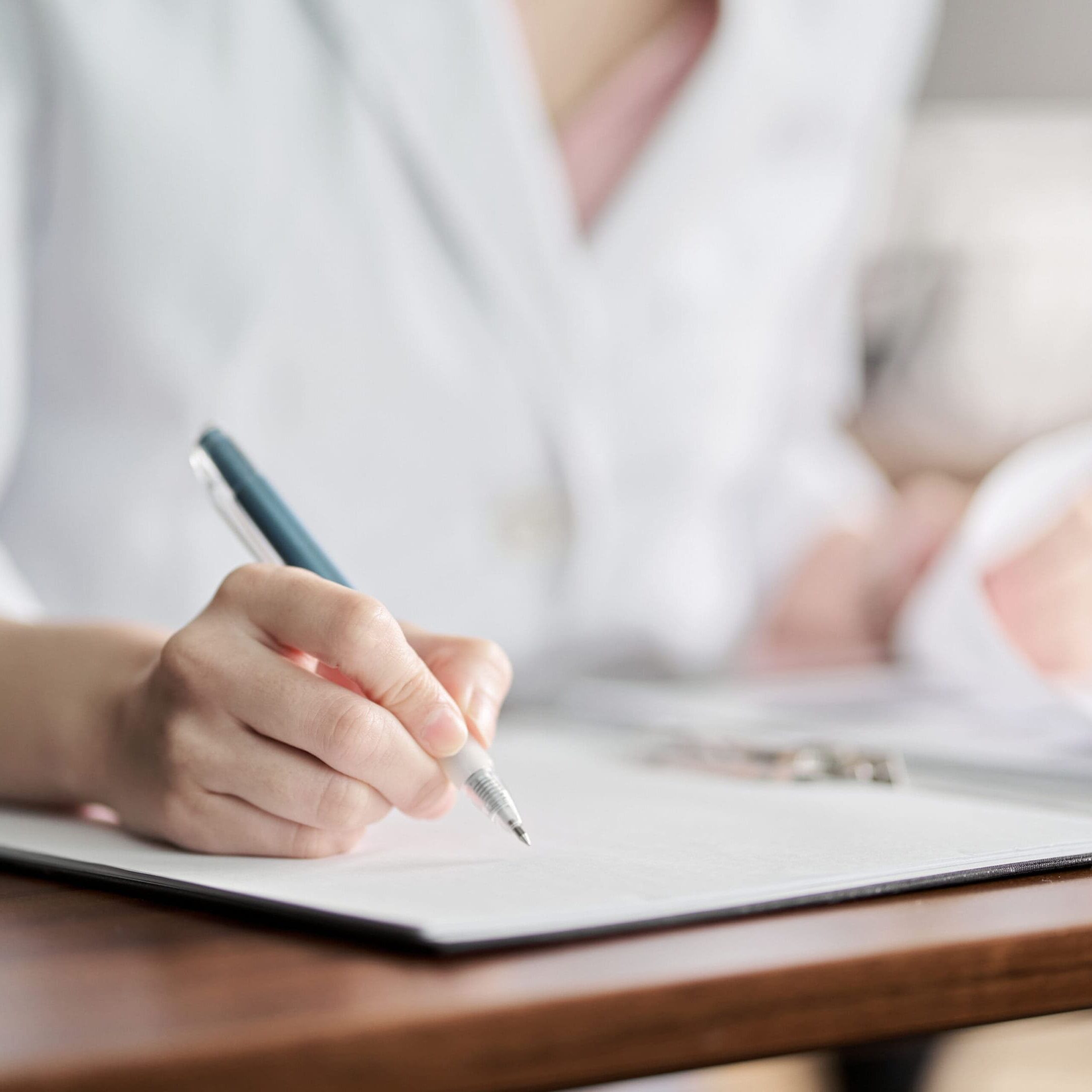 A person writing on paper with pen and pencil.